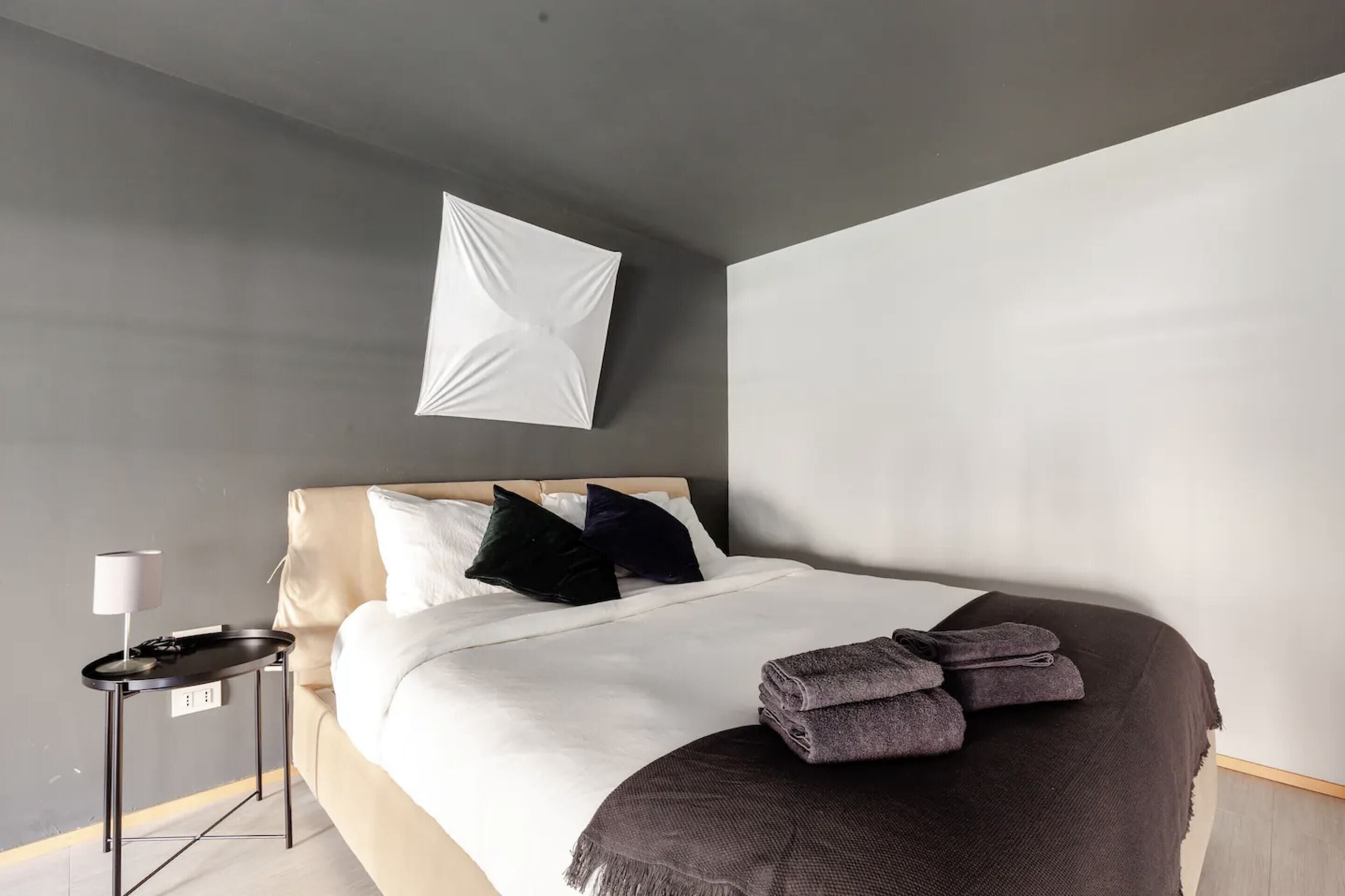 Une chambre d’hôtel moderne avec un lit soigneusement fait, une petite table de chevet avec une lampe et un luminaire fixé au mur.