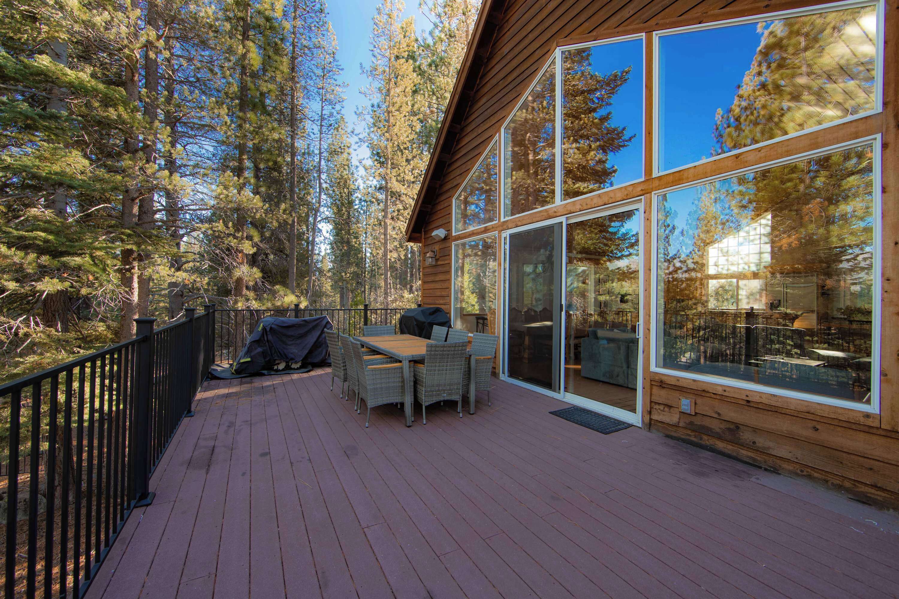 A wooden deck with a table and chairs, surrounded by tall trees.