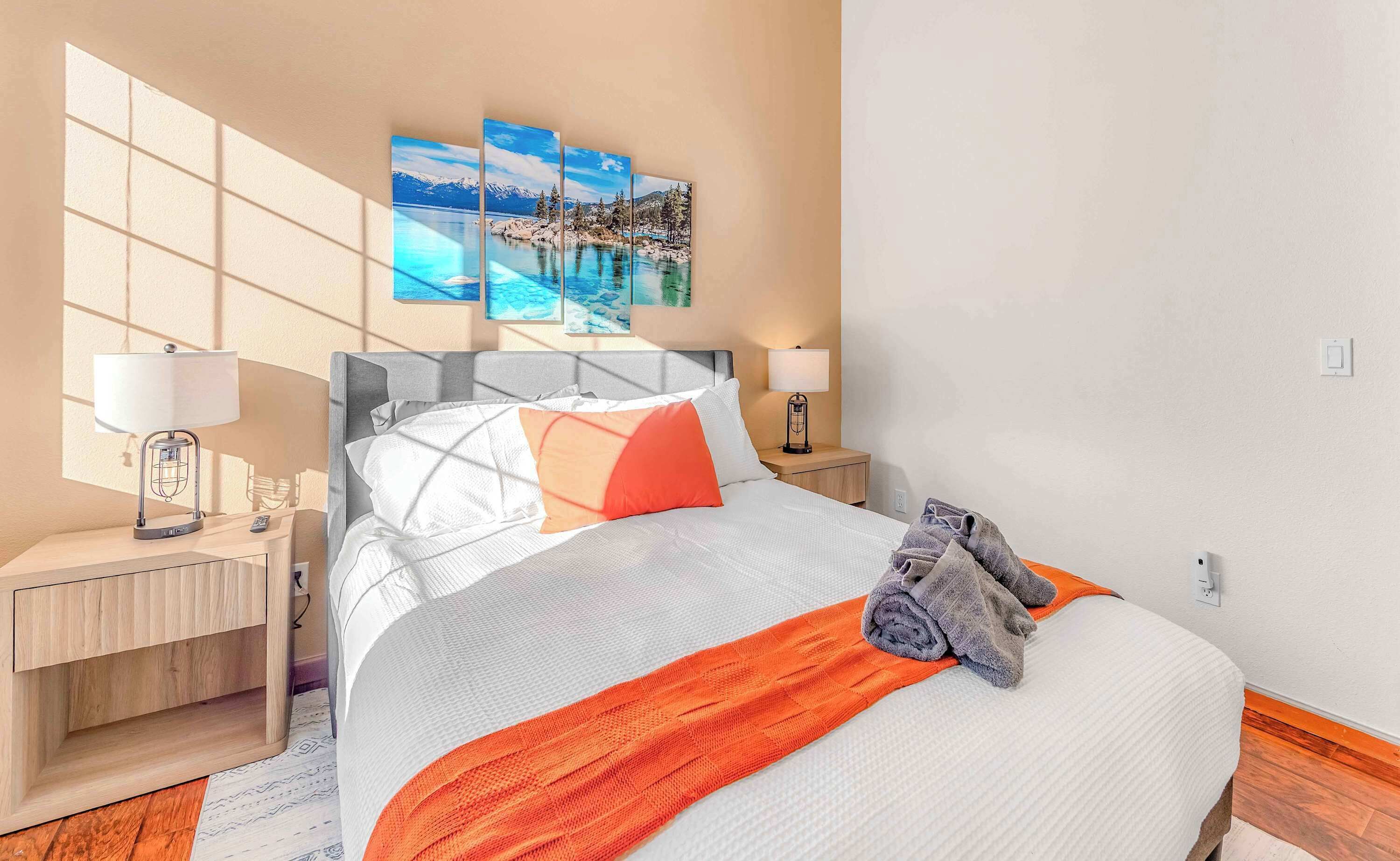 A hotel room with a bed, two bedside tables, a lamp, a painting, and a window.