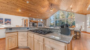 Une cuisine spacieuse dotée d’un grand îlot central, d’un plafond en bois et de grandes fenêtres offrant une vue sur l’extérieur.