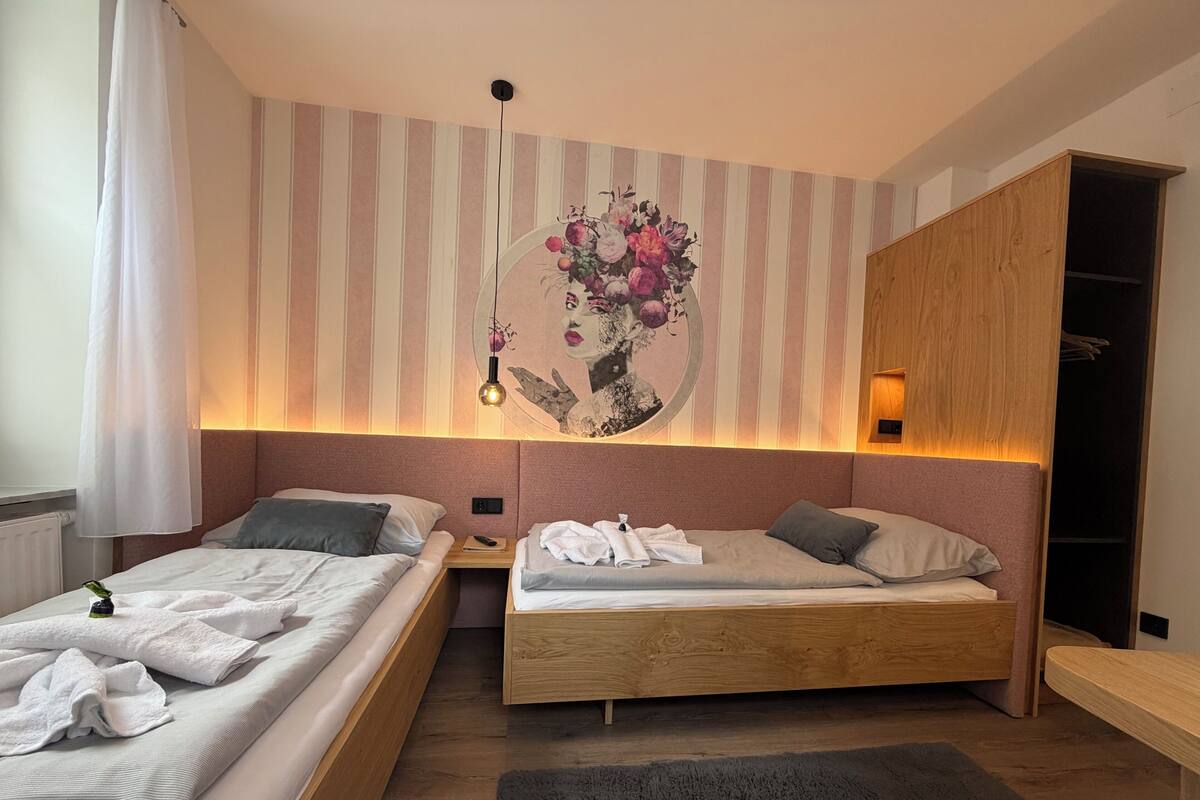 A modern bedroom with two beds, a wooden headboard, a nightstand, a wall-mounted light, and a decorative floral mural.