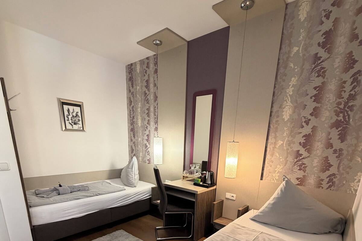 A hotel room with two beds, a desk, a chair, a mirror, and a framed picture on the wall.