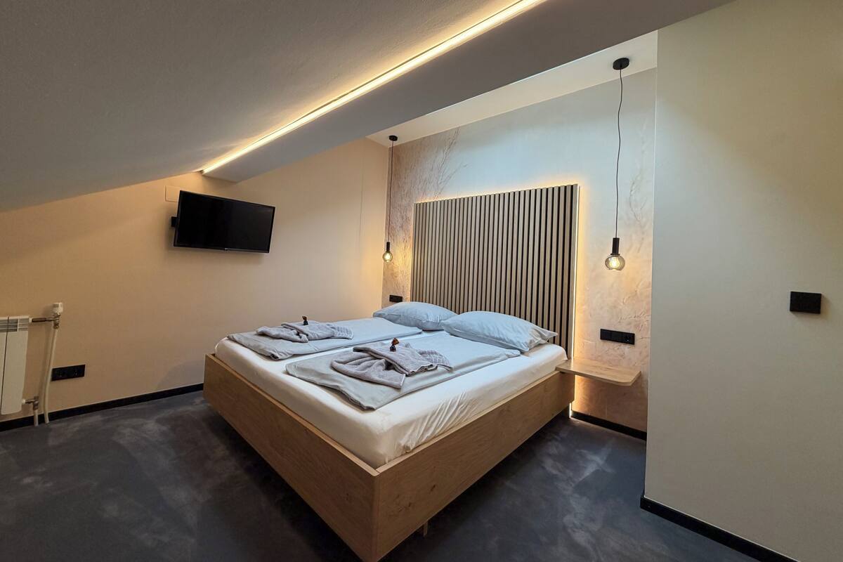 A modern bedroom with a wooden bed, a mounted TV, and a wall-mounted light fixture.