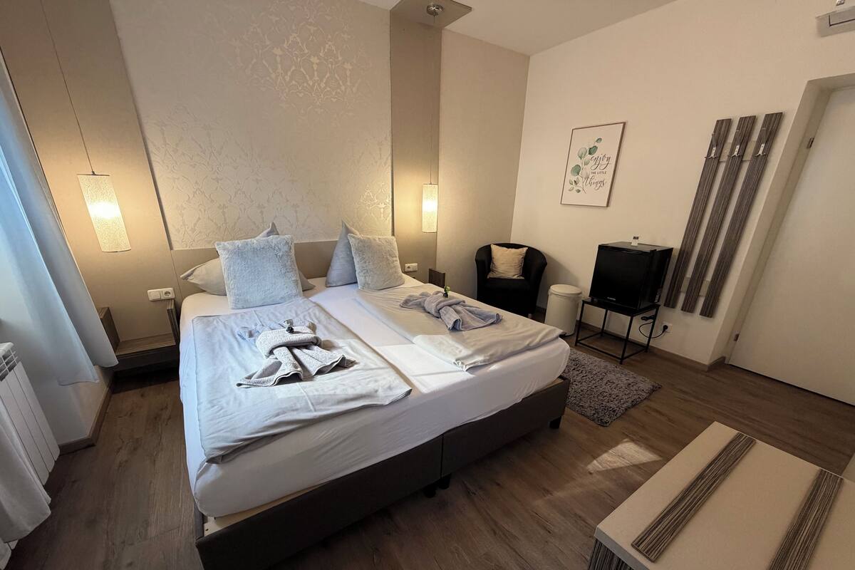 A modern hotel room with a large bed, bedside lamps, a chair, a TV, and a wall with a framed quote.