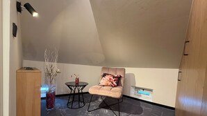 Una stanza moderna e accogliente, con soffitto alto, un tavolo rotondo, una poltrona imbottita, un armadietto in legno e un vaso con rami secchi.