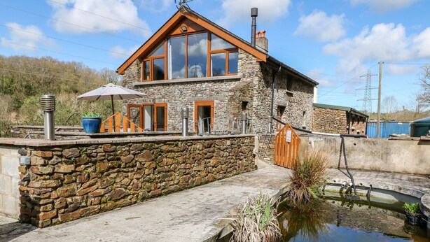 A stone house with a pond, wooden deck, and a large window. - Monkleigh Mill (Bideford)