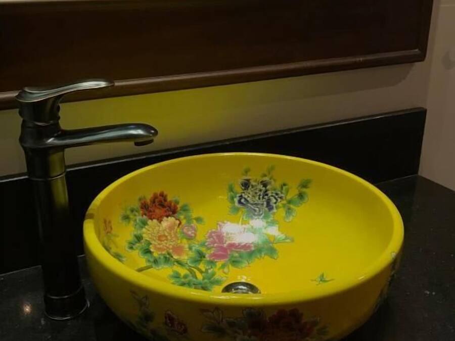A yellow sink with floral designs, a black faucet, and a mirror above it.