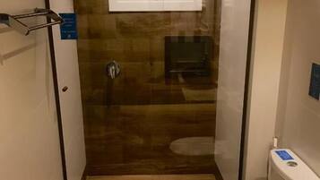 Baño compacto con cabina de ducha, inodoro y una pequeña ventana sobre la ducha.