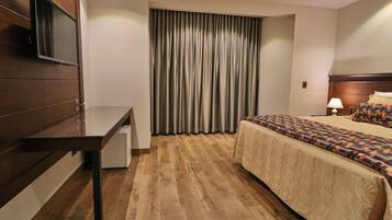 Una habitación de hotel con cama, escritorio, televisión y ventana con cortinas.