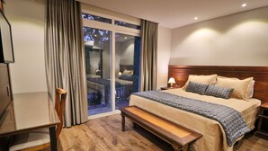Una habitación de hotel con una cama grande, un banco de madera, un escritorio y vistas por una puerta corrediza de vidrio.