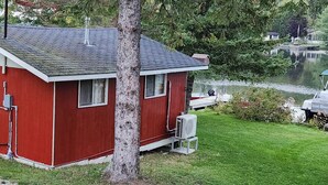 Eine kleine, rote Holzhütte mit geneigtem Dach, einem Propangasbehälter und einer Klimaanlage.
