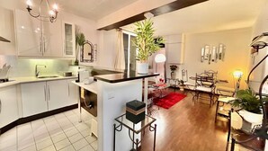 A modern kitchen with white cabinets, a black countertop, and a central island. There is a dining area with a red rug and metal chairs. - Center of Paris - Aladdin's house (Paris)