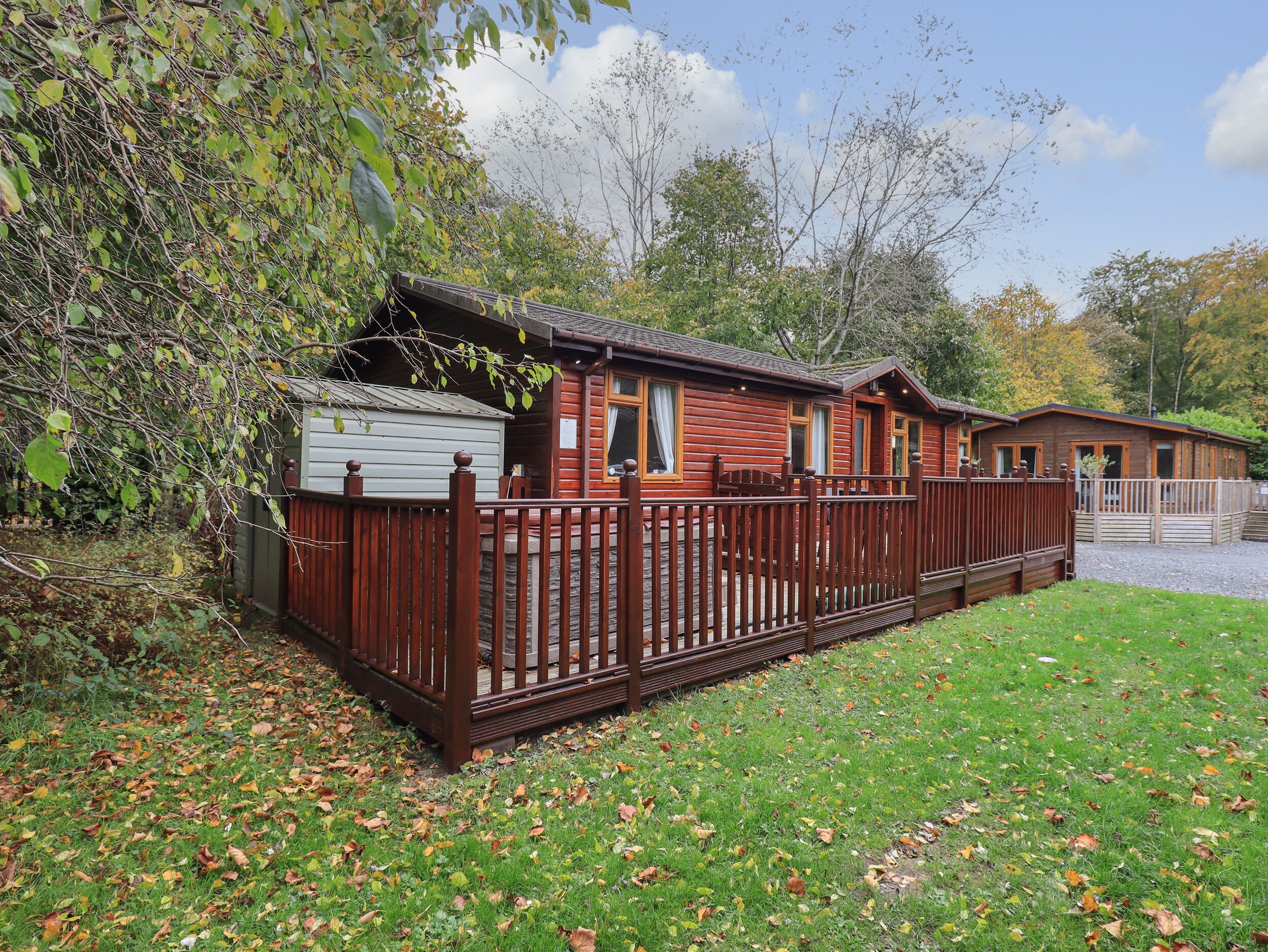 A wooden cabin with a fenced deck, surrounded by trees and a grassy area.