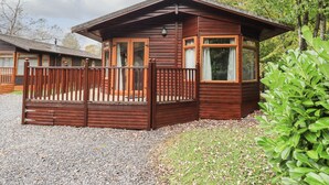 A wooden cabin with a porch, a fenced yard, and a gravel driveway. - Cedar Lodge (Windermere)