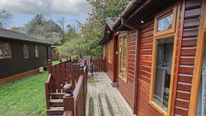 A wooden deck with a railing, a small table, and a bench. - Cedar Lodge (Windermere)