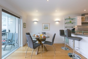 A modern dining area with a glass table, grey chairs, and a bar counter with stools. - The Waves (St Ives)