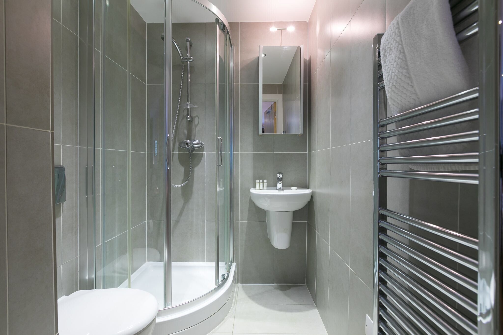 A modern bathroom with a glass-enclosed shower, a white sink, and a towel rack.