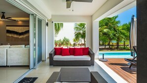 Una sala de estar moderna con un sofá, un ventilador de techo y vistas a una piscina y palmeras.
