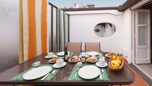 Une table à manger dressée pour le petit-déjeuner, avec des assiettes, des tasses et un saladier rempli de fruits.
