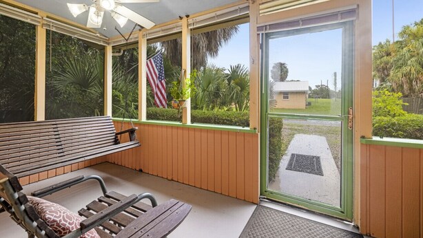 Eine überdachte Veranda mit Deckenventilator, einer Bank, einem Tisch und Blick auf ein Haus und Grünflächen.