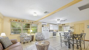 Ein geräumiges Wohnzimmer mit einer braunen Ledersofa, gemusterten Sesseln, einem Holztisch und einem Essbereich mit Tisch und Stühlen.