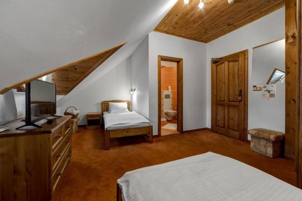 Ein Schlafzimmer mit schrägen Wänden, Holzmöbeln, einem Bett, einer Kommode, einem Fernseher und einem kleinen Fenster.