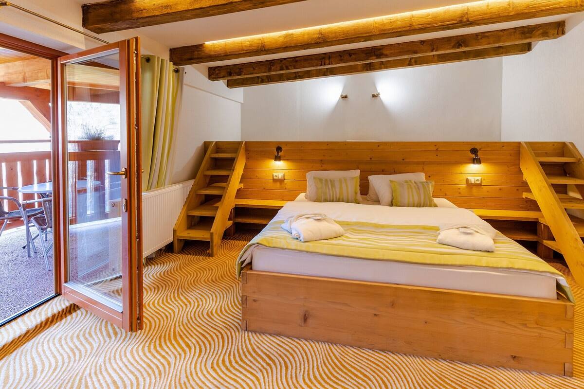 Ein Schlafzimmer mit einem hölzernen Bett, einem Fenster mit Vorhängen, einer Holztreppe und Blick ins Freie.