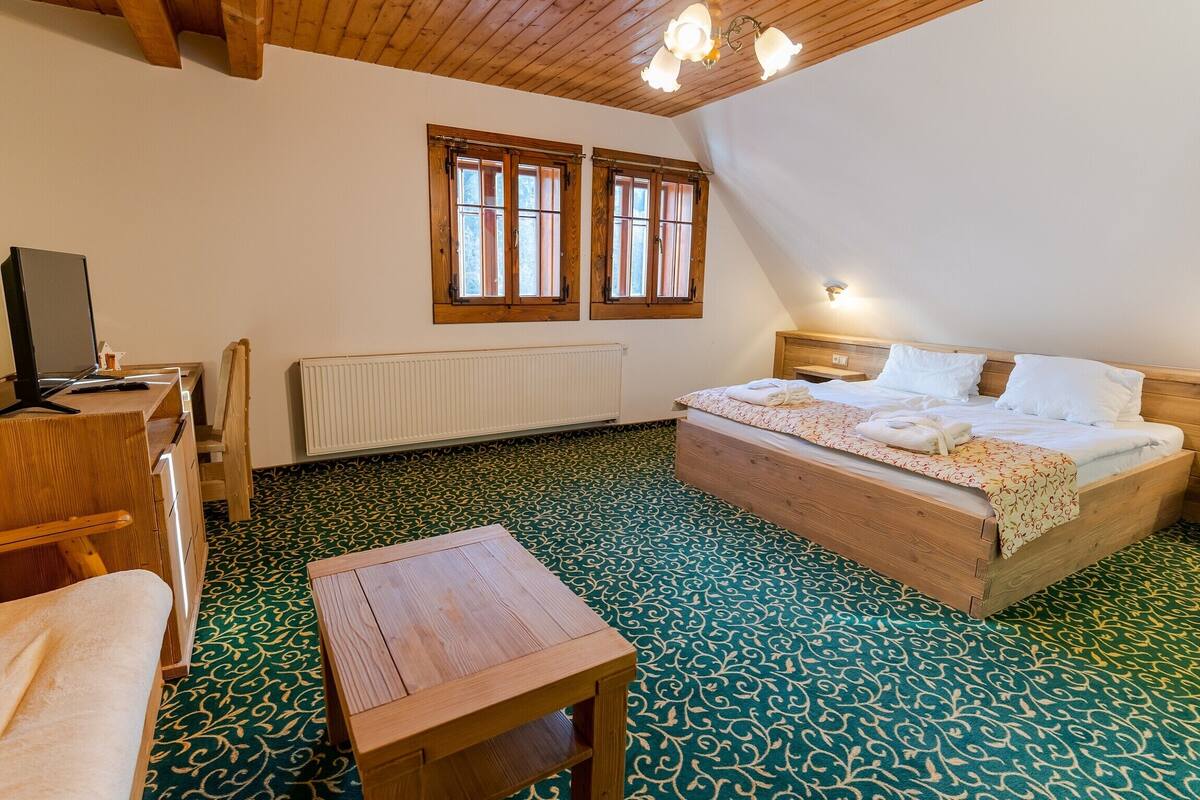 Ein Schlafzimmer mit einem hölzernen Bett, einem Schreibtisch, einem Stuhl, einer Heizung und zwei Fenstern.