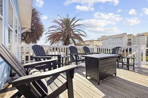 A deck with outdoor furniture, a table, and a palm tree. - Charlie's Beach Retreat | Fun 4BR w/ Heated Pool (North Myrtle Beach)