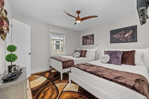 A bedroom with two beds, a ceiling fan, a window, and artwork on the walls. - Charlie's Beach Retreat | Fun 4BR w/ Heated Pool (North Myrtle Beach)
