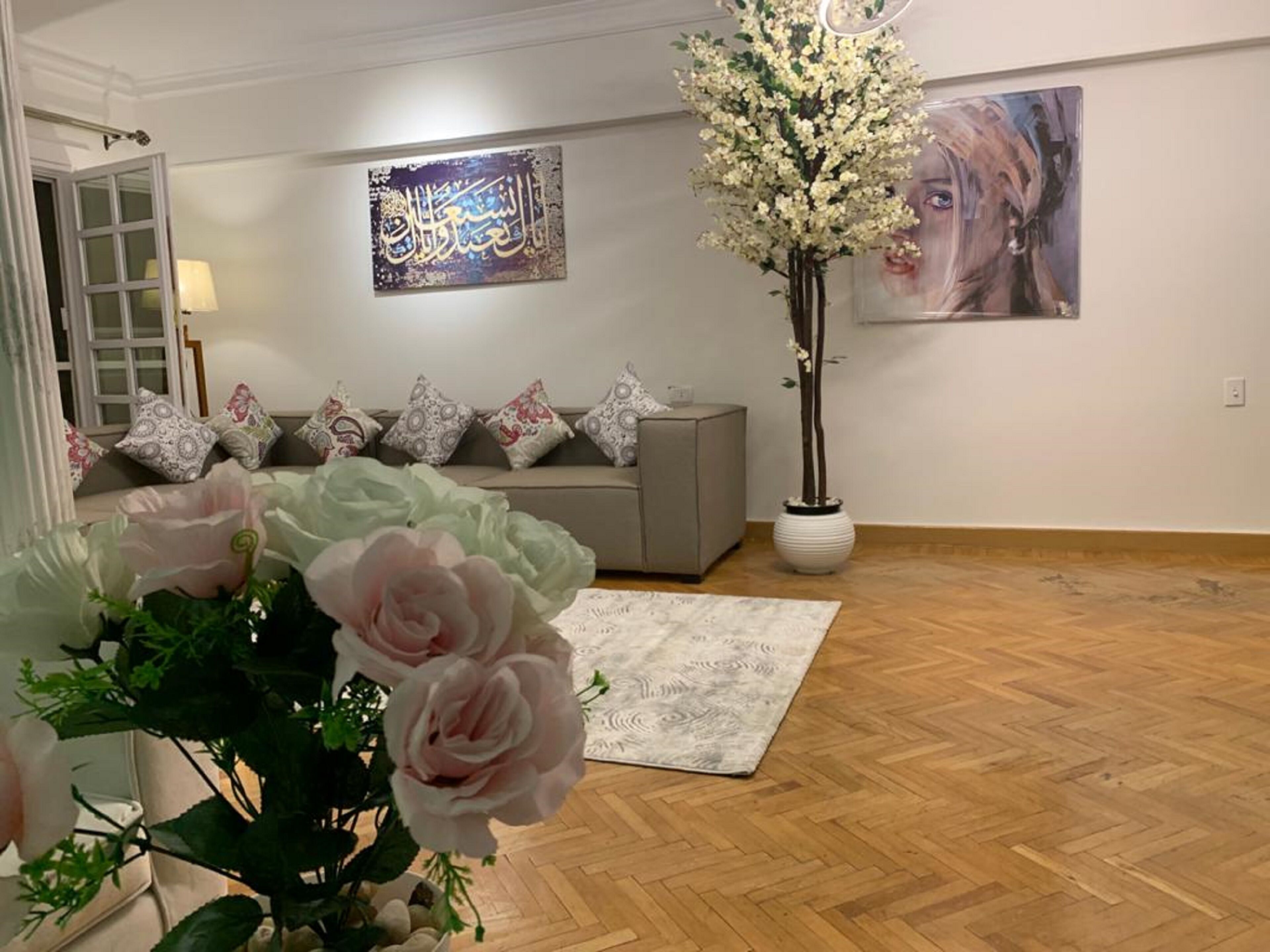 Una sala de estar con un sofá, cojines decorativos, un arreglo floral grande y obras de arte en las paredes.