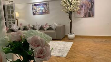 Una sala de estar con un sofá, cojines decorativos, un arreglo floral grande y obras de arte en las paredes.