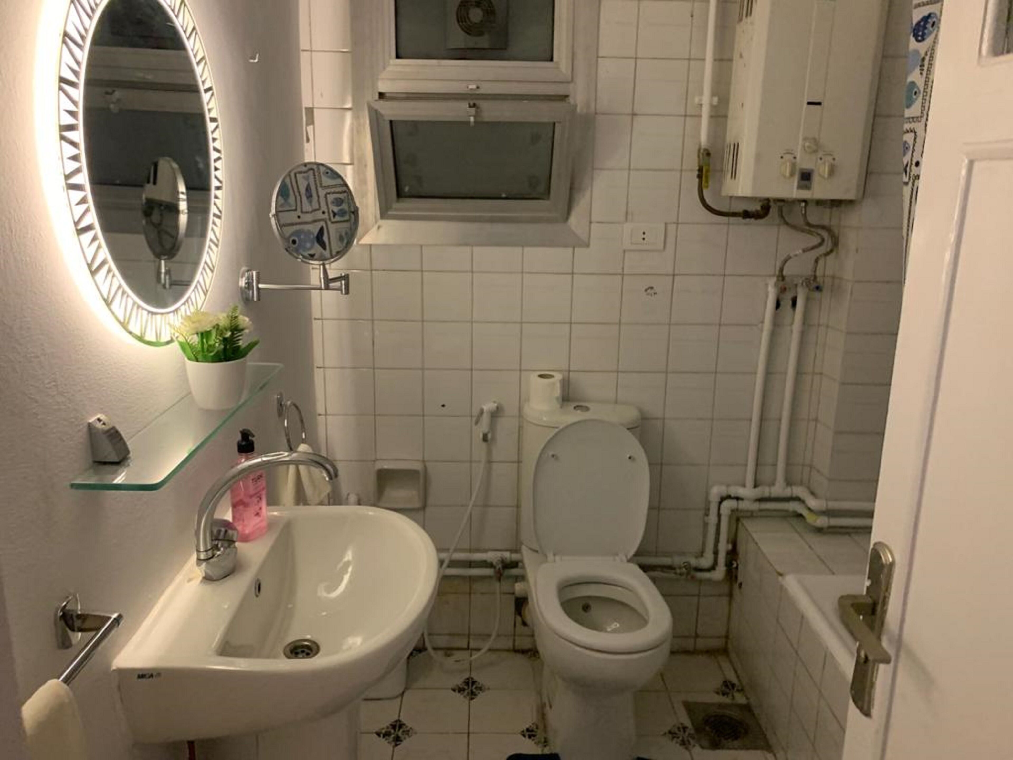 A bathroom with a sink, mirror, toilet, and a small window above the toilet.