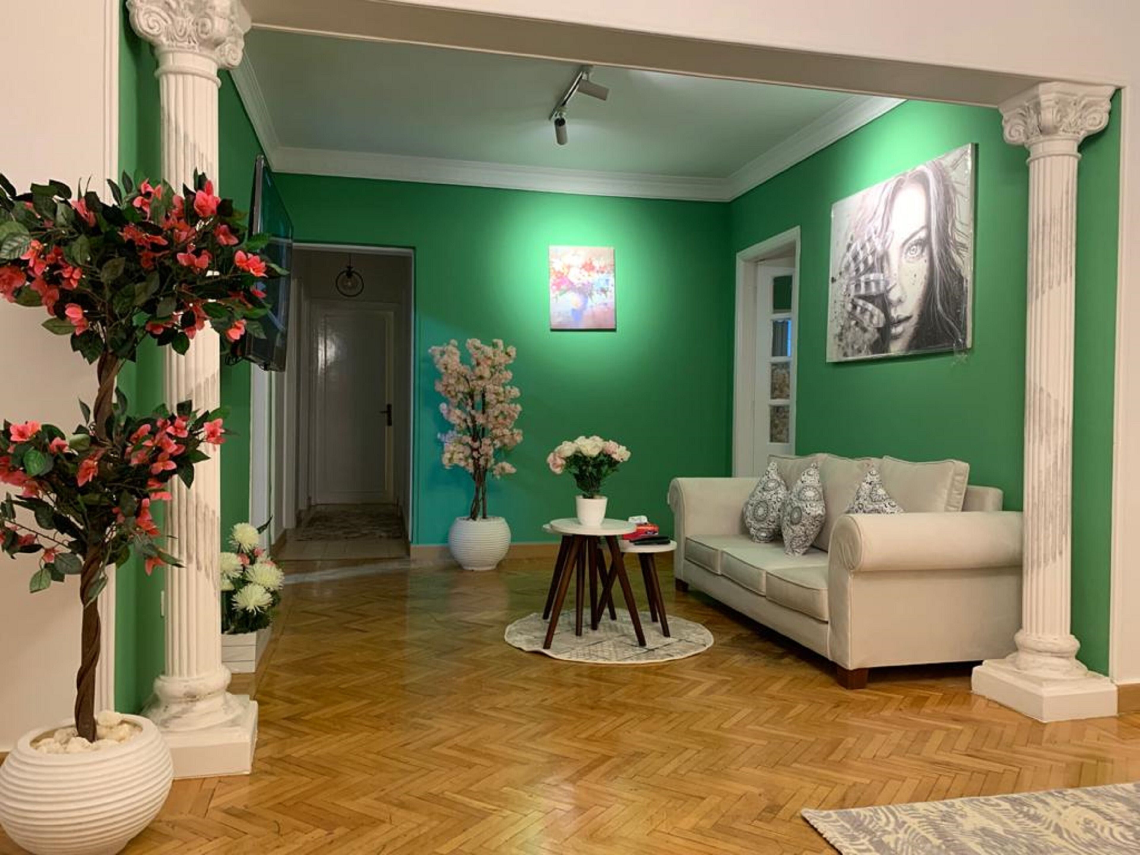Ein Wohnzimmer mit grüner Wand, weißen Säulen, einem weißen Sofa und Holzboden.