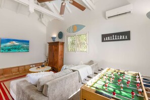 Una habitación con mesa de futbolín, sofá, armario, televisor y ventana con vista al océano.