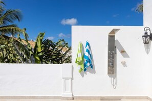 Pared blanca con una reja de metal, un aplique y un perchero con toallas a rayas.