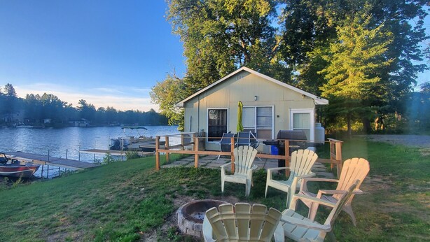 Una cabaña junto al lago con muelle, mobiliario exterior y un bote.