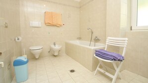 Un baño con inodoro, bidé, bañera y una silla con toallas.