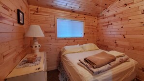 Una camera in una casetta di legno con un letto, un comodino, una lampada e una finestra.