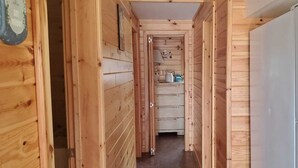 Un corridoio di legno stretto con un frigorifero bianco sulla destra, armadietti in legno e una piccola finestra in fondo.