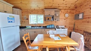 Una cucina in stile chalet con pareti in legno, un frigorifero, un lavello, un fornello e un tavolo da pranzo con sedie.