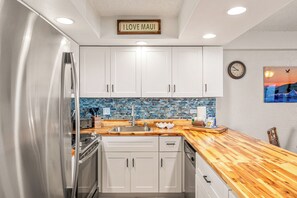 A kitchen with white cabinets, a wooden countertop, a stainless steel refrigerator, and a blue-tiled backsplash.