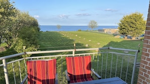 Un balcon avec deux chaises à rayures rouges et une table, donnant sur un espace verdoyant avec vue sur la mer.