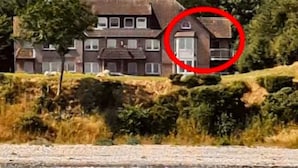 Une maison à deux étages avec une cheminée bien visible, située près d’une étendue d’eau.
