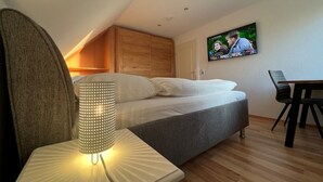 Une chambre à coucher moderne, avec un lit, une lampe de chevet, un téléviseur fixé au mur et un bureau en bois avec une chaise.
