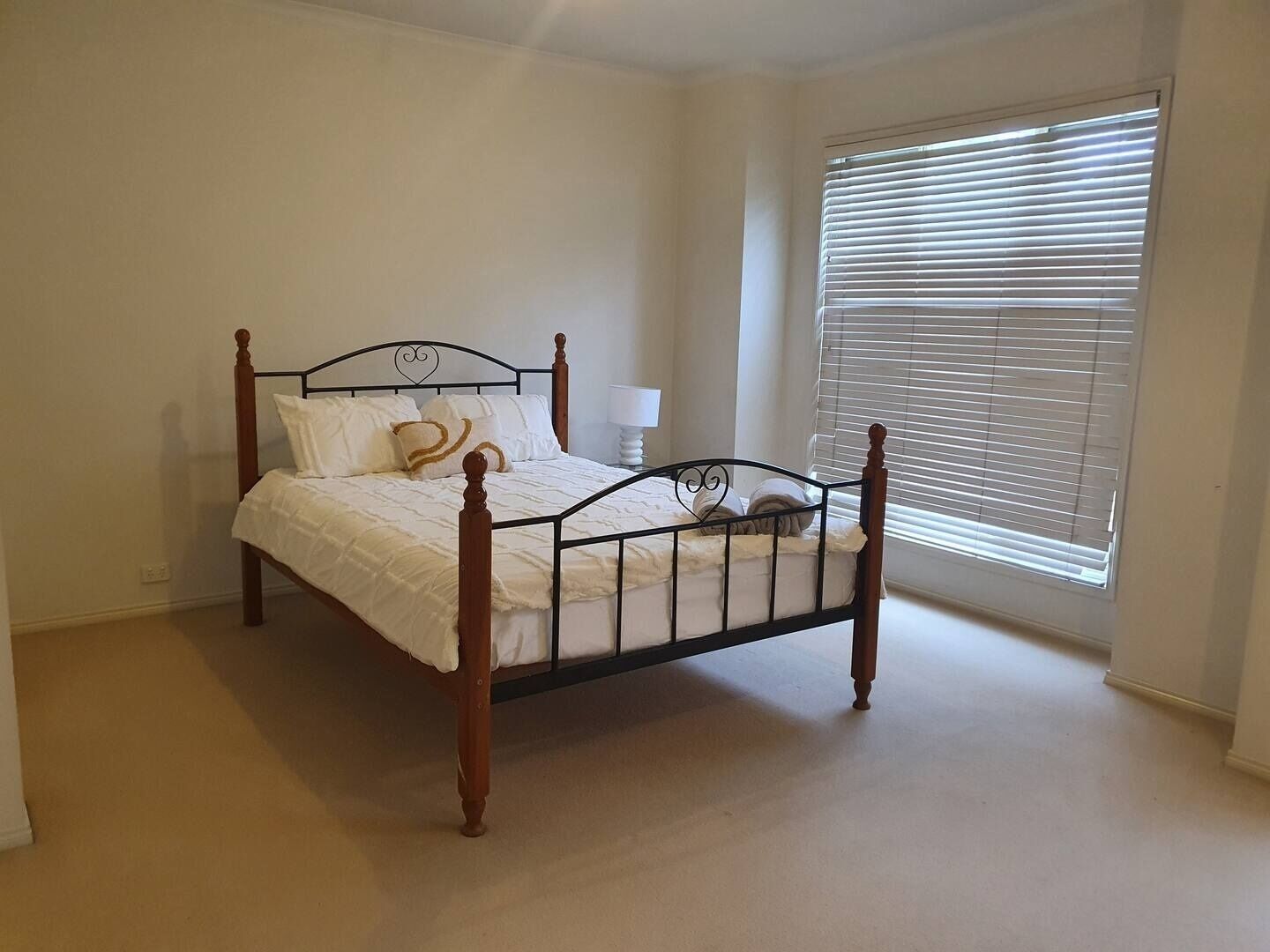 Ein Schlafzimmer mit einem Einzelbett, einem Fenster mit Jalousien und einem Nachttisch mit Lampe.