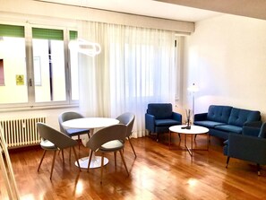 A modern living room with a wooden floor, a round table with four chairs, two blue sofas, and a floor lamp. - Sprone Apartment in Firenze (Florence)