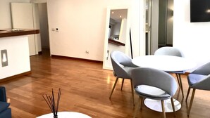 Ein moderner Essbereich mit einem runden Tisch und vier Stühlen, im Hintergrund eine Küche und ein Flachbildfernseher an der Wand.