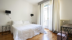 Ein Schlafzimmer mit einem Bett, zwei an der Wand befestigten Fernsehern, einem Tisch und einer Bank.