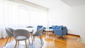 Ein modernes Wohnzimmer mit rundem Couchtisch, zwei Sofas und einem Essbereich mit Stühlen.